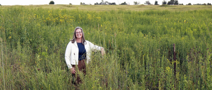 women in black shirt & white jacket standing in a field do wildflowers (Woods Prairie Preserve)