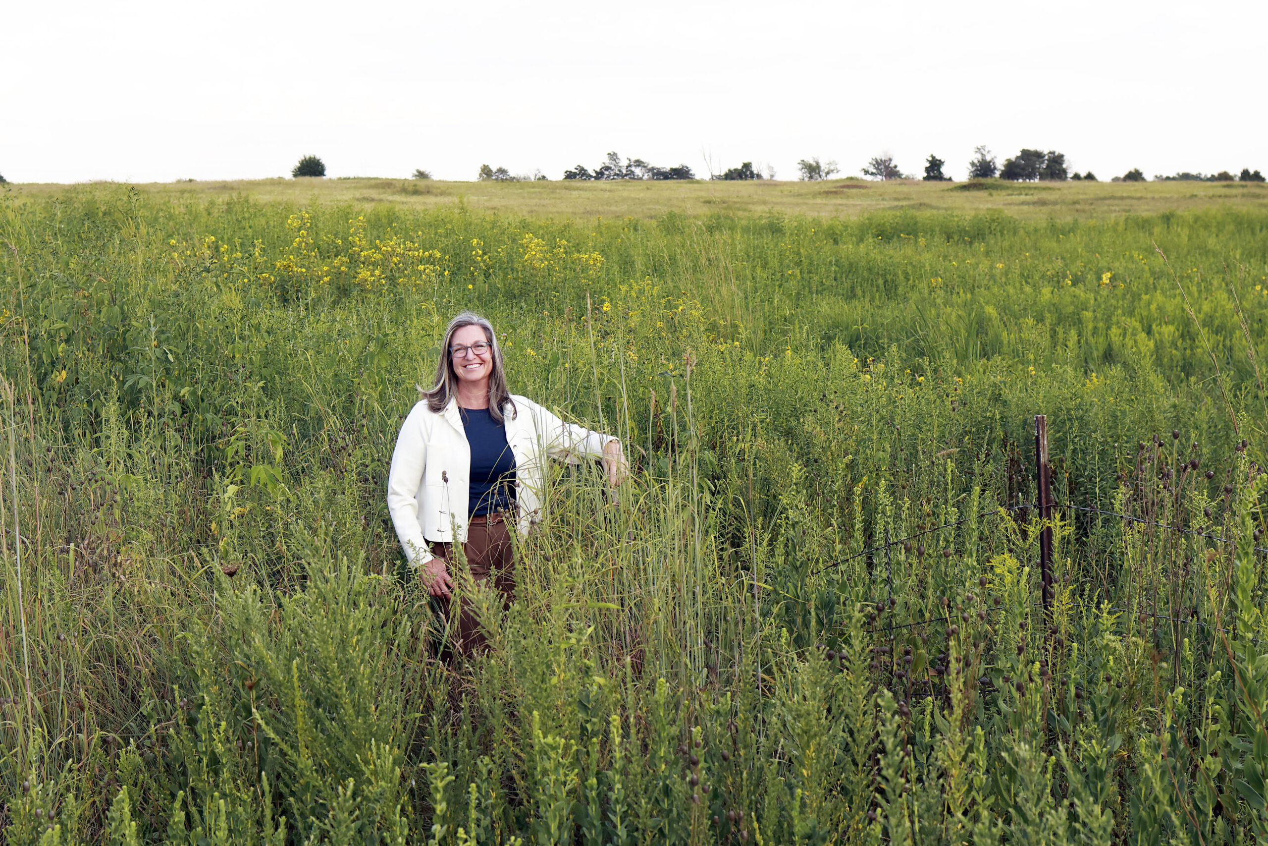 women in black shirt & white jacket standing in a field do wildflowers (Woods Prairie Preserve)